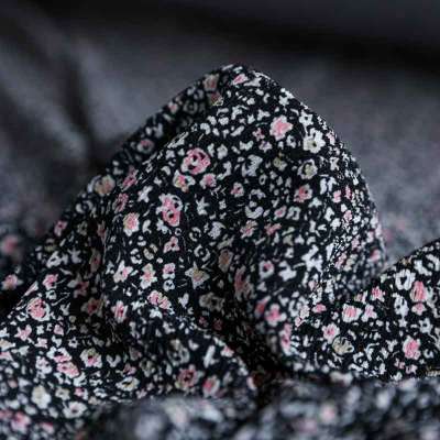 Tissu fibranne viscose noir avec motif floral rose et blanc.